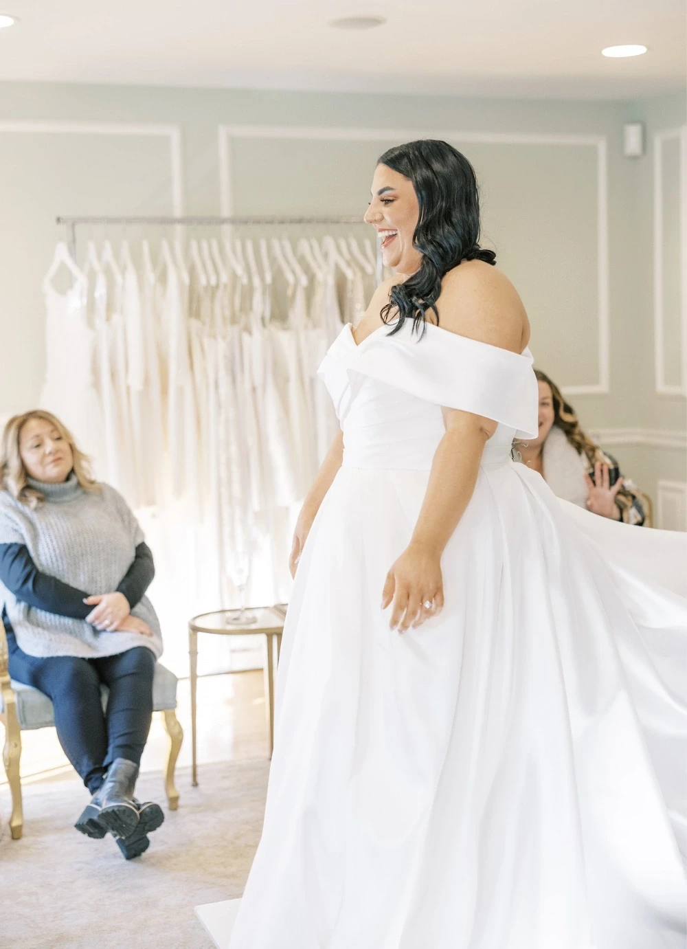Bride smiling in off-shoulder gown with family watching